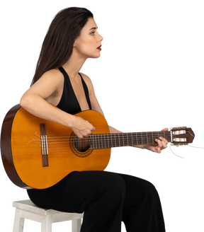 坐着的年轻女子，穿着黑色西装，抱着吉他，放在一边的四分之三的视图