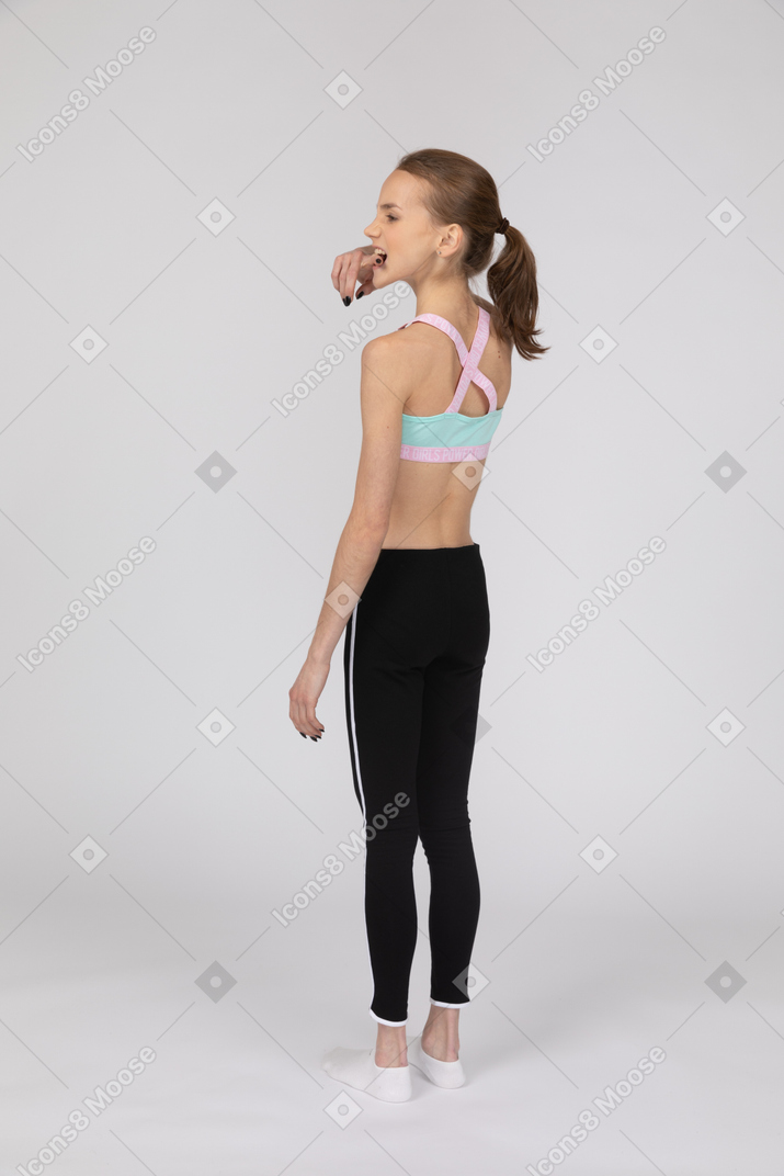 Three-quarter back view of a teen girl in sportswear biting her finger