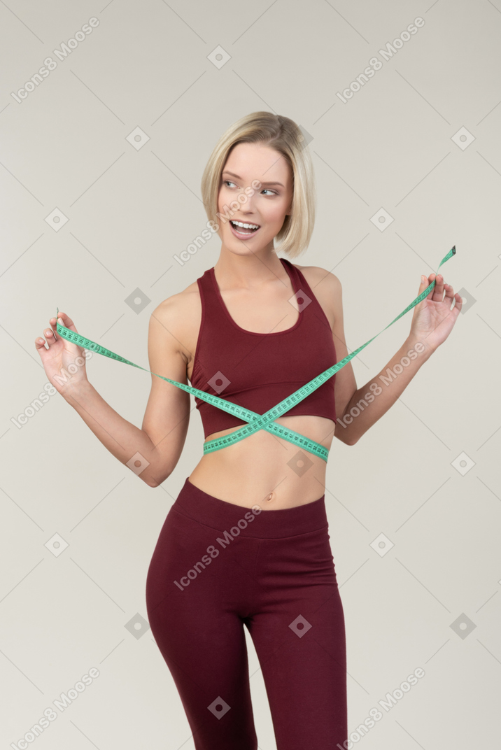 Положительная молодая женщина в спортивной одежде измеряет талию