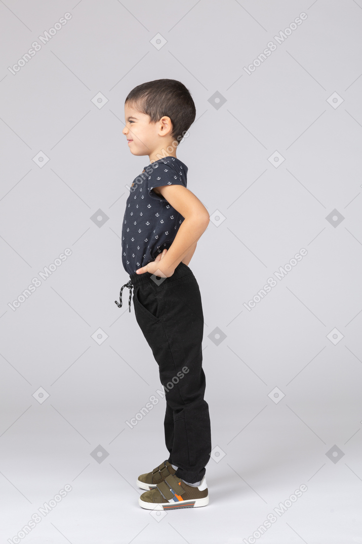 Side view of a cute boy in casual clothes posing with hands on hips