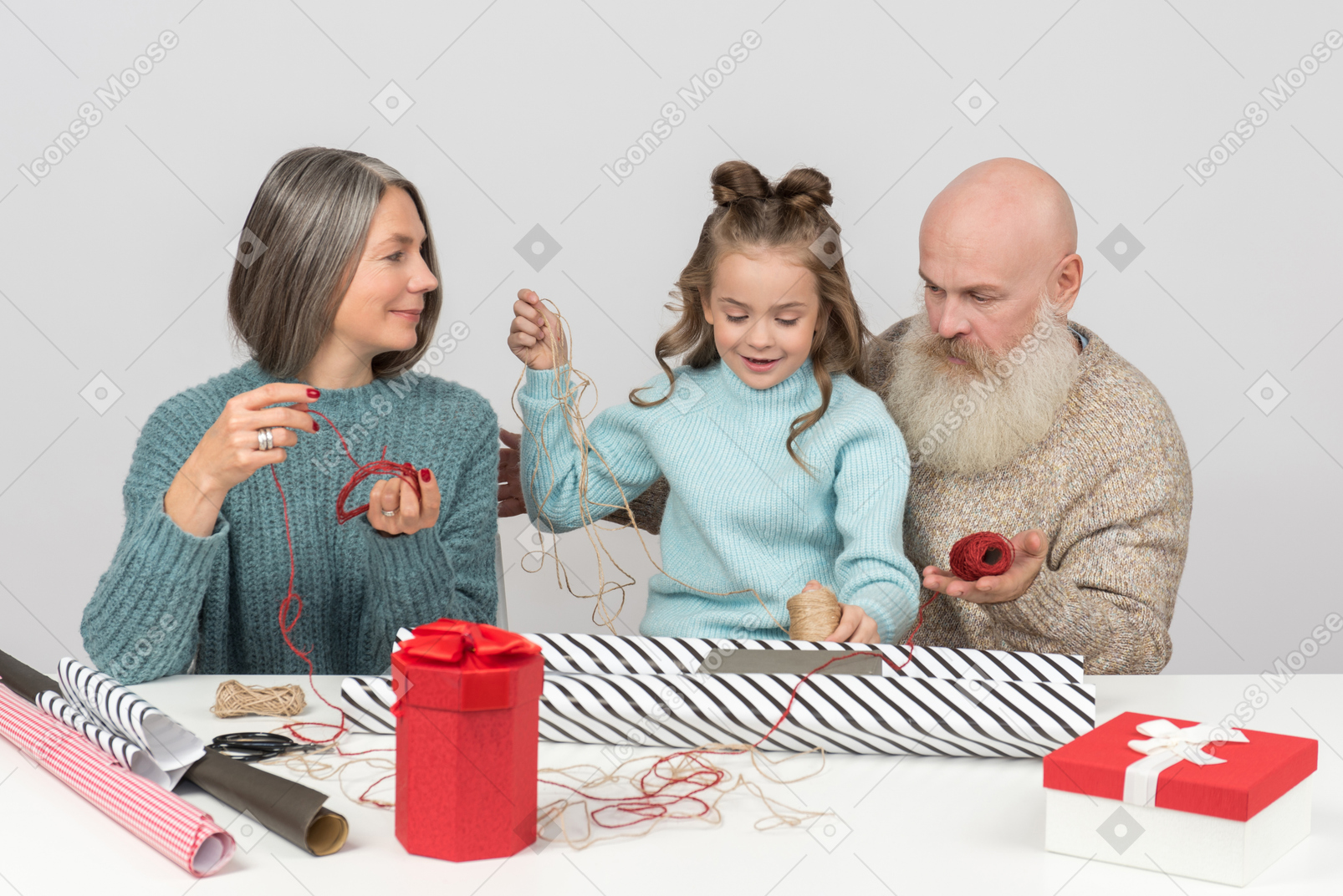 Бабушка и дедушка и внучка упаковывают рождественские подарки