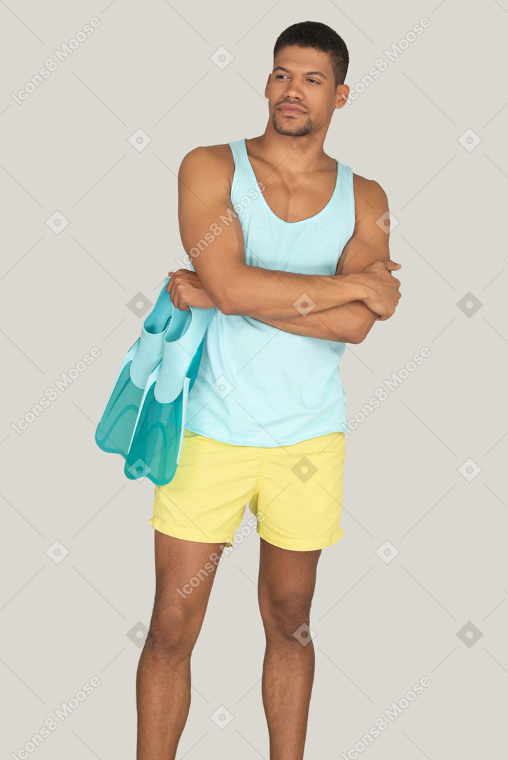 Man in blue tank top and yellow shorts holding flippers