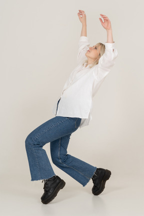 Vista lateral de uma mulher loira em roupas casuais dançando na ponta dos pés e levantando as mãos