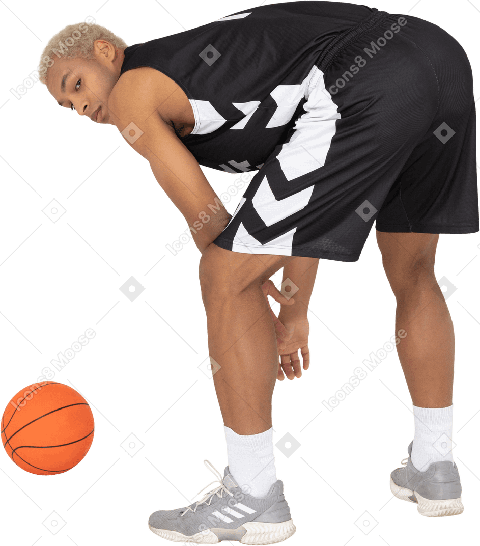 一名年轻男篮球运动员站在球旁的四分之三后视图