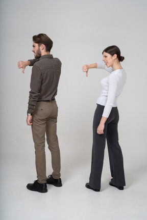 Vista posterior de tres cuartos de una pareja joven en ropa de oficina mostrando el pulgar hacia abajo