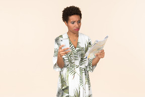 Black short-haired woman in a white and green dress, standing with a smartphone in her hand