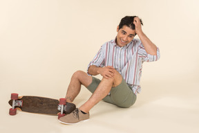 Young caucasian guy adjusting hair and sitting near skate