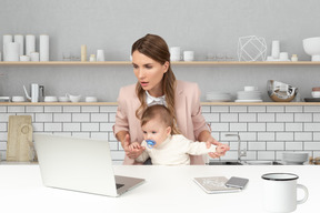 A woman holding a baby while looking at a laptop