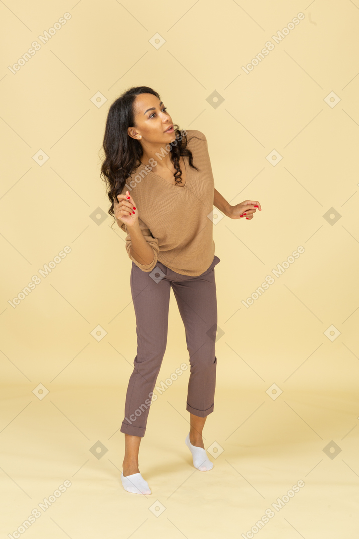 Three-quarter view of a dancing dark-skinned young female raising hands