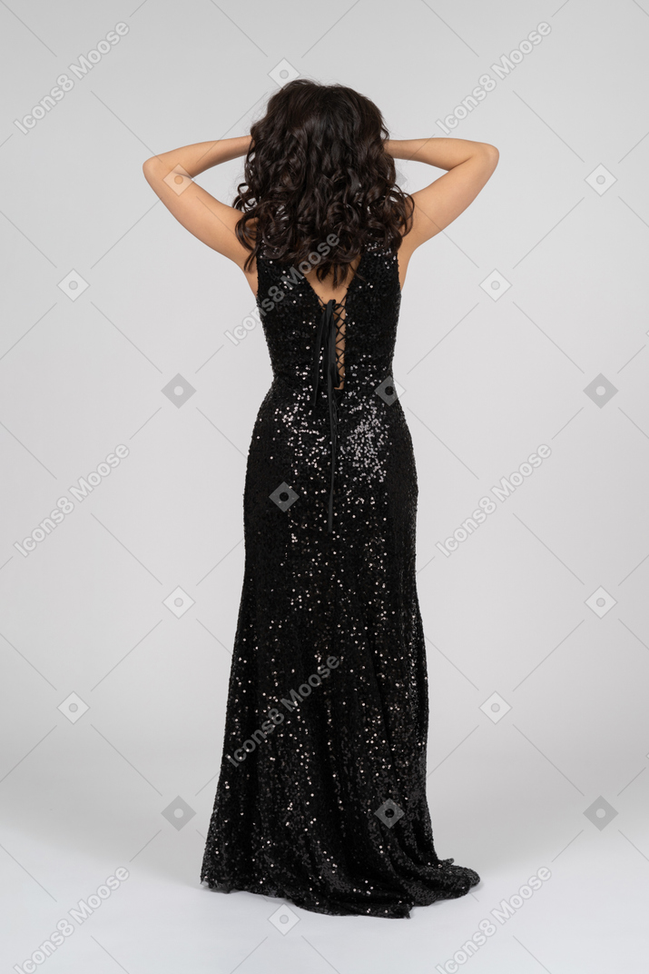 Woman in black evening dress standing back to camera and holding head