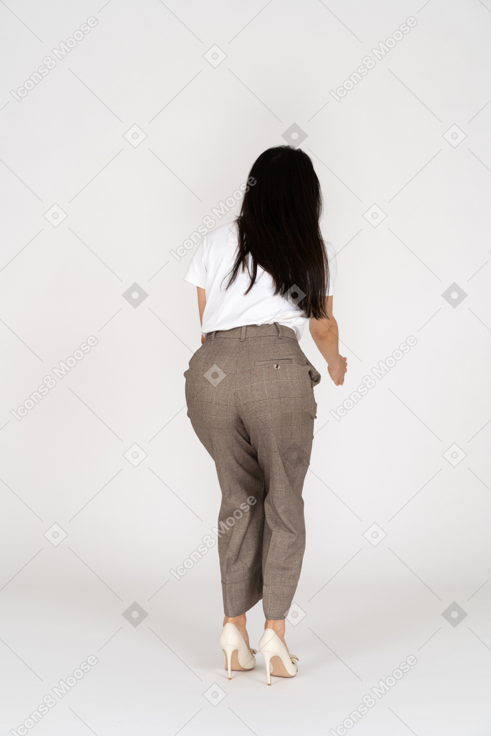 Vista posteriore di una giovane donna in calzoni e t-shirt che allunga la mano e si china