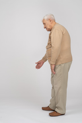 Side view of an old man in casual clothes standing with extended arm