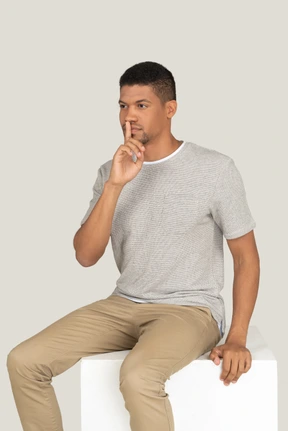 A good looking beautiful man sitting on the white chair and making silence gesture