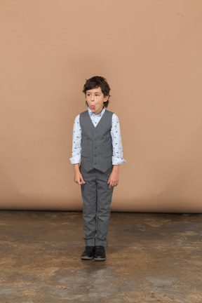 一个穿着灰色西装的可爱男孩站着不动做鬼脸的前视图