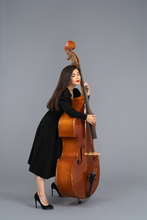Side view of a young female musician in black dress holding her double-bass