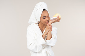 Black woman in white bathrobe and head towel enjoying her skin care routine