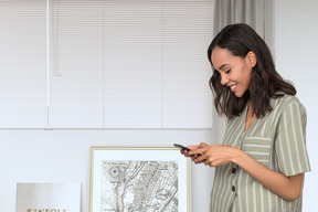 A woman standing next to a window looking at her cell phone