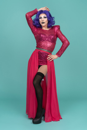 Drag queen in pink dress posing with one hand on hip and the other on top of head