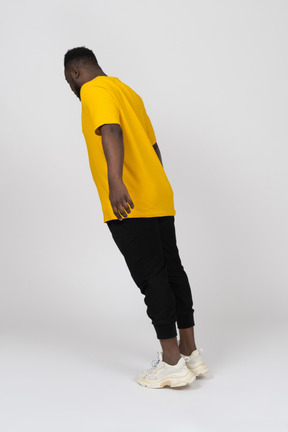Vista de três quartos das costas de um jovem de pele escura em uma camiseta amarela, inclinando-se para a frente e estendendo o braço