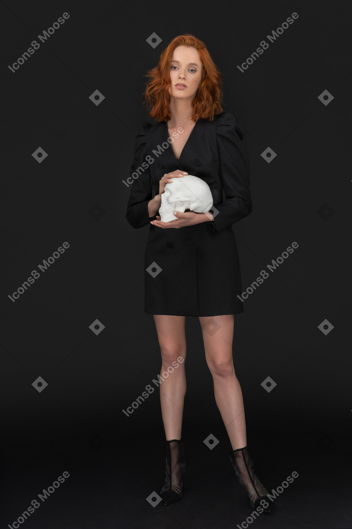 A frontal view of the sexy elegant woman holding a skull and looking to the camera