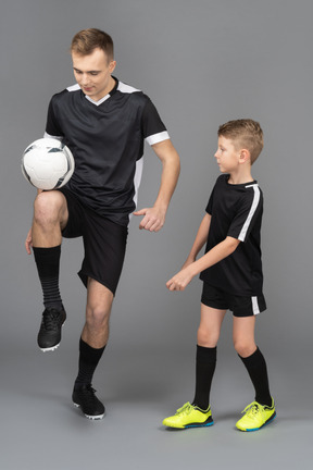 In voller länge von einem jungen mann, der einem kleinen jungen beibringt, wie man fußball spielt