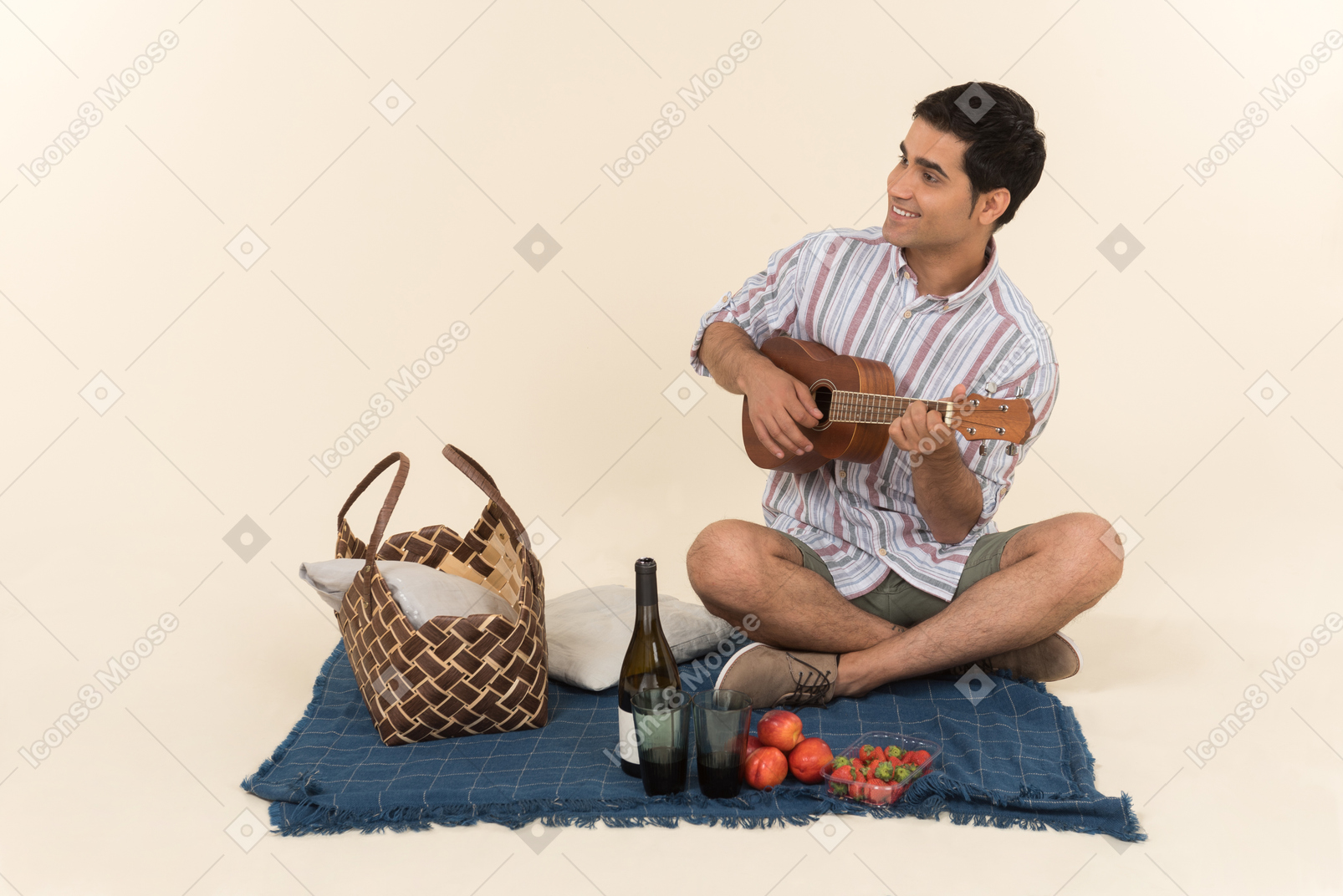 Chico caucásico joven sentado en una manta y tocando la guitarra pequeña