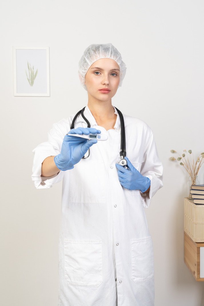 Front view of a young female doctor with stethoscope holding thermometer