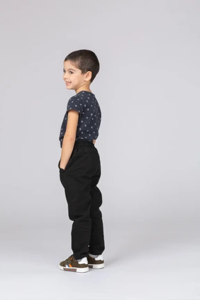 Side view of a happy boy in casual clothes posing with hands in pockets