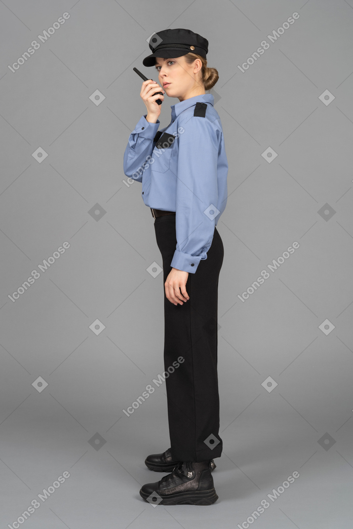 Female security officer standing in profile and using walkie-talkie
