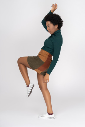 Active african girl lifting one leg and hand in profile