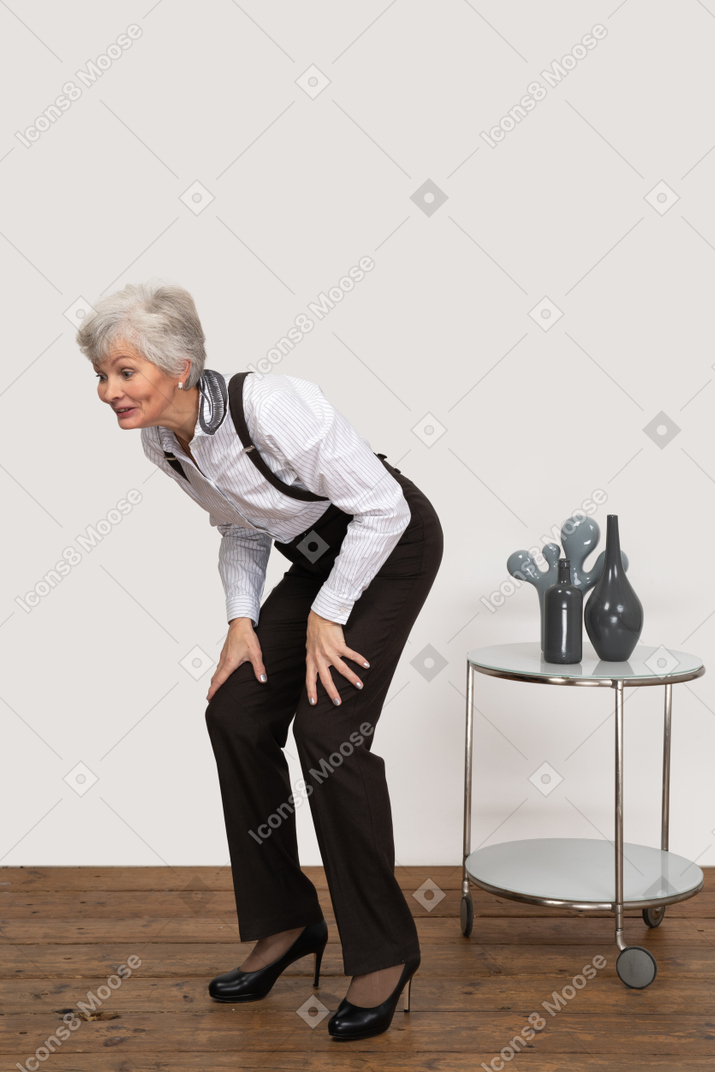 Vue de trois quarts d'une vieille dame accroupie mettant les mains sur les jambes
