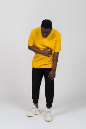 Vista frontal de um jovem de pele escura em uma camiseta amarela tocando o estômago