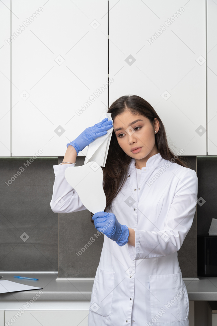 Front view of a female doctor looking at the mirror and wiping her forehead