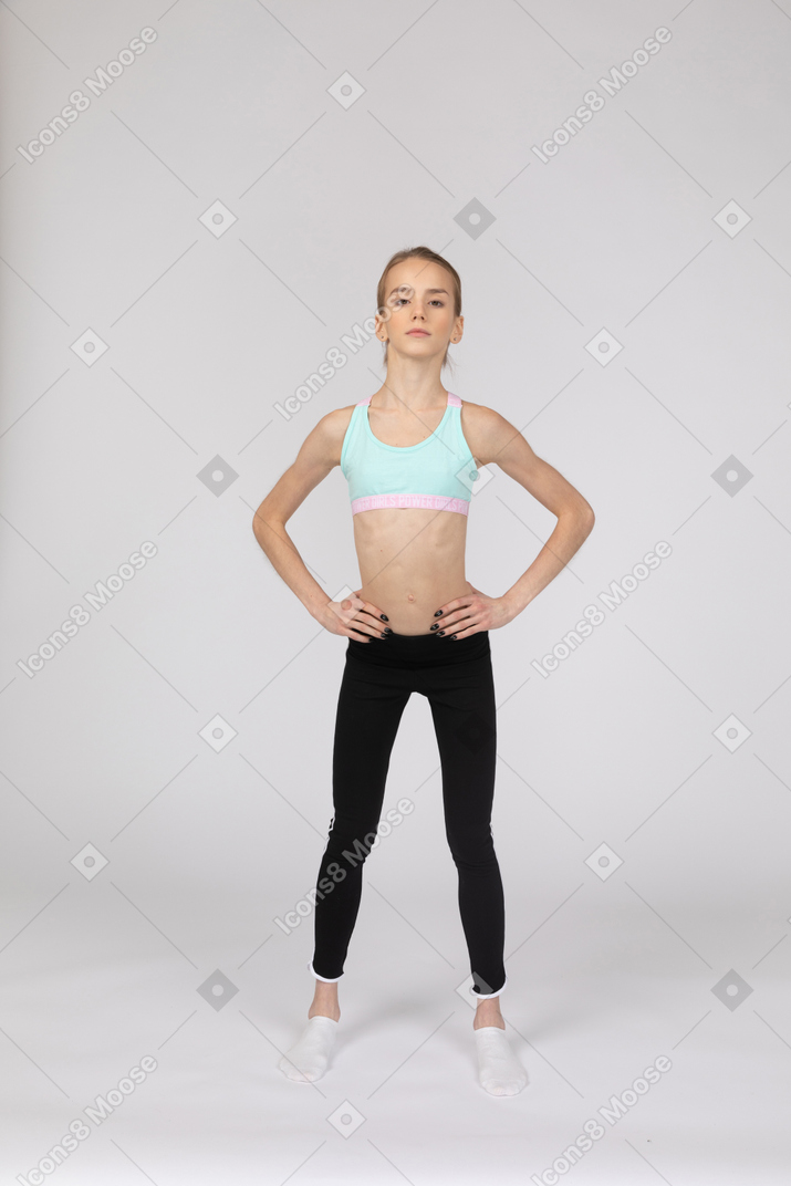 一个十几岁的女孩，将手放在臀部上的运动服的前视图