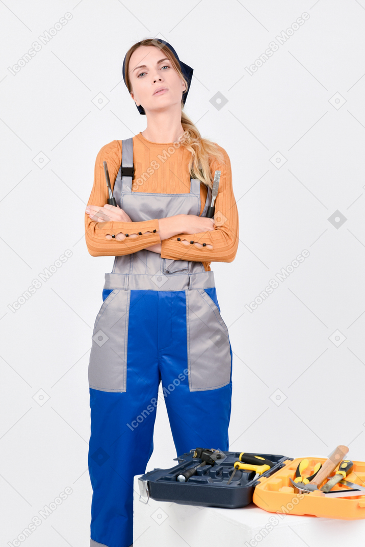 Female plumber standing next to bag with tools with her hands folded