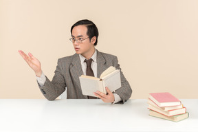 An asian teacher in a checkered suit, a tie and a book in his hand, working with the class