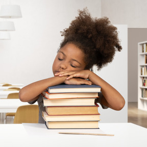 A young girl leaning her head on a stack of books