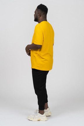 Three-quarter back view of a young dark-skinned man in yellow t-shirt holding hands together