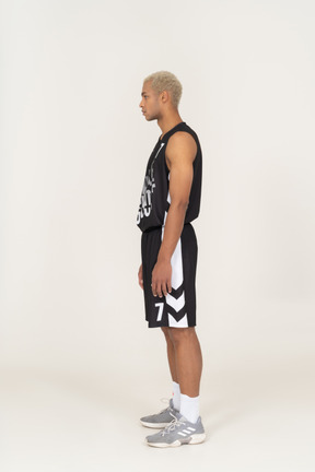 Vista laterale di un giovane giocatore di basket maschile in piedi immobile e guardando da parte