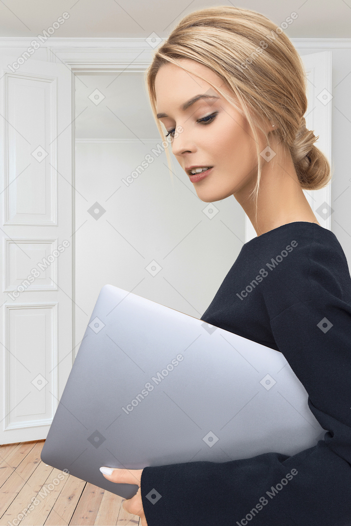 A woman in a business suit holding a laptop in an empty room