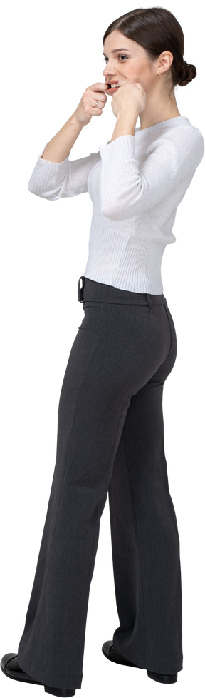 Three-quarter back view of a young woman in office clothing stretching mouth