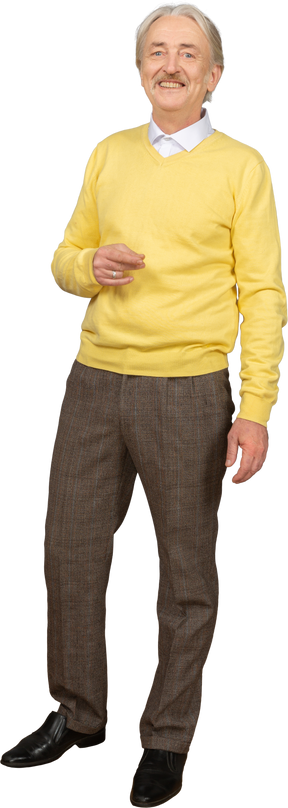 黄色のプルオーバーを着て、笑顔でカメラを見ている身振りで示す老人の正面図