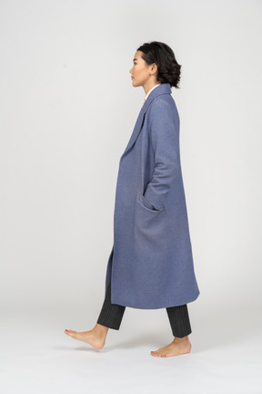 Side view of woman in coat walking barefoot