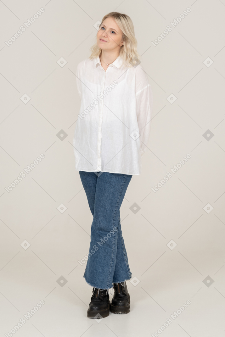 Vista frontale di una donna bionda timida in abiti casual gambe incrociate e guardando da parte