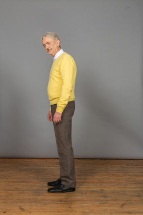 Vista laterale di un vecchio uomo che indossa un pullover giallo chinandosi e guardando la fotocamera