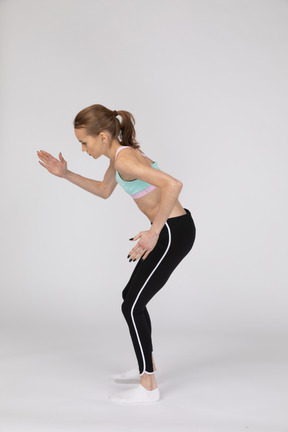 Vista lateral de una jovencita en ropa deportiva inclinada hacia adelante mientras está de pie como un robot