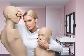 A woman standing next to two mannequins in a bathroom