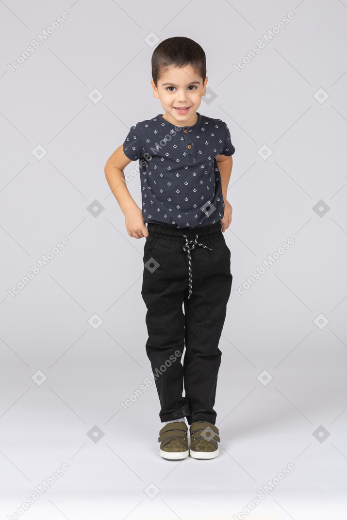 Front view of a happy boy standing with hands on hips and looking at camera