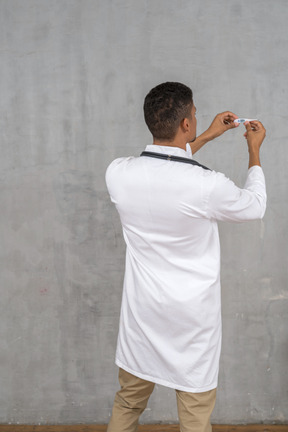 Back view of a male doctor holding a thermometer