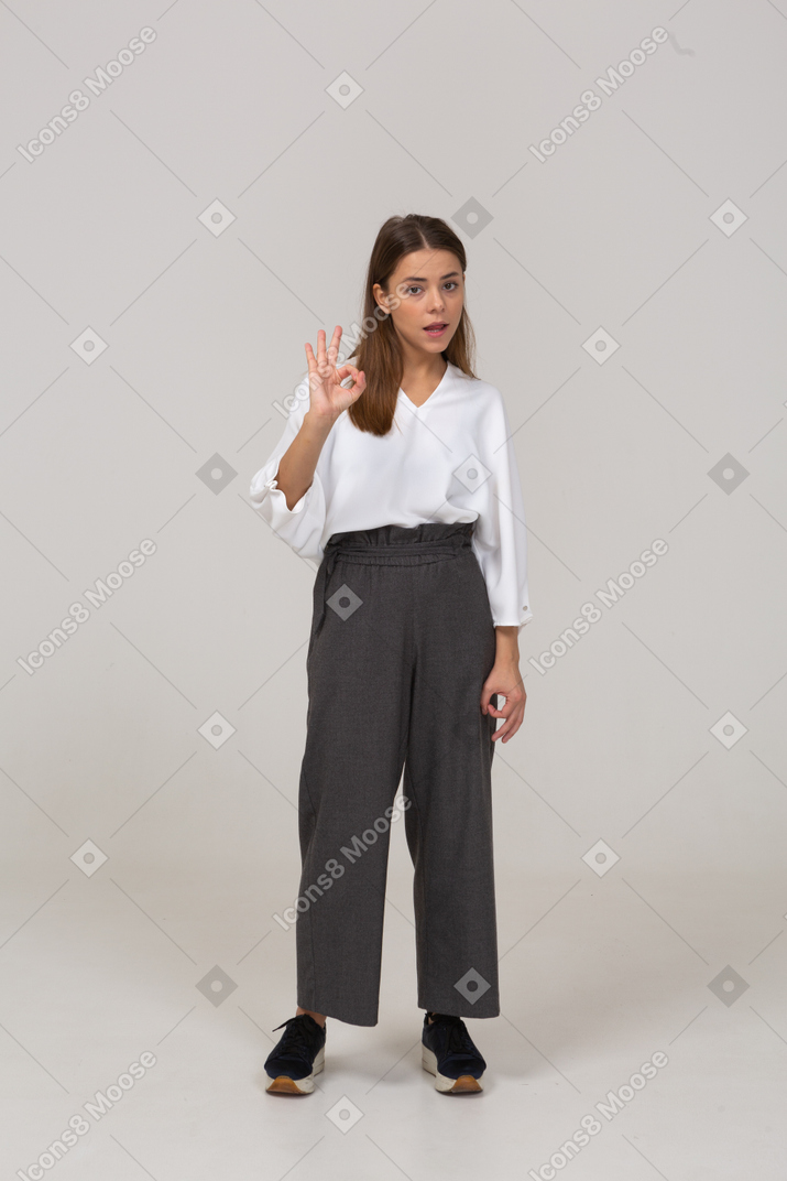 Трехчетвертный вид молодой леди в офисной одежде, показывающей жест "ок"